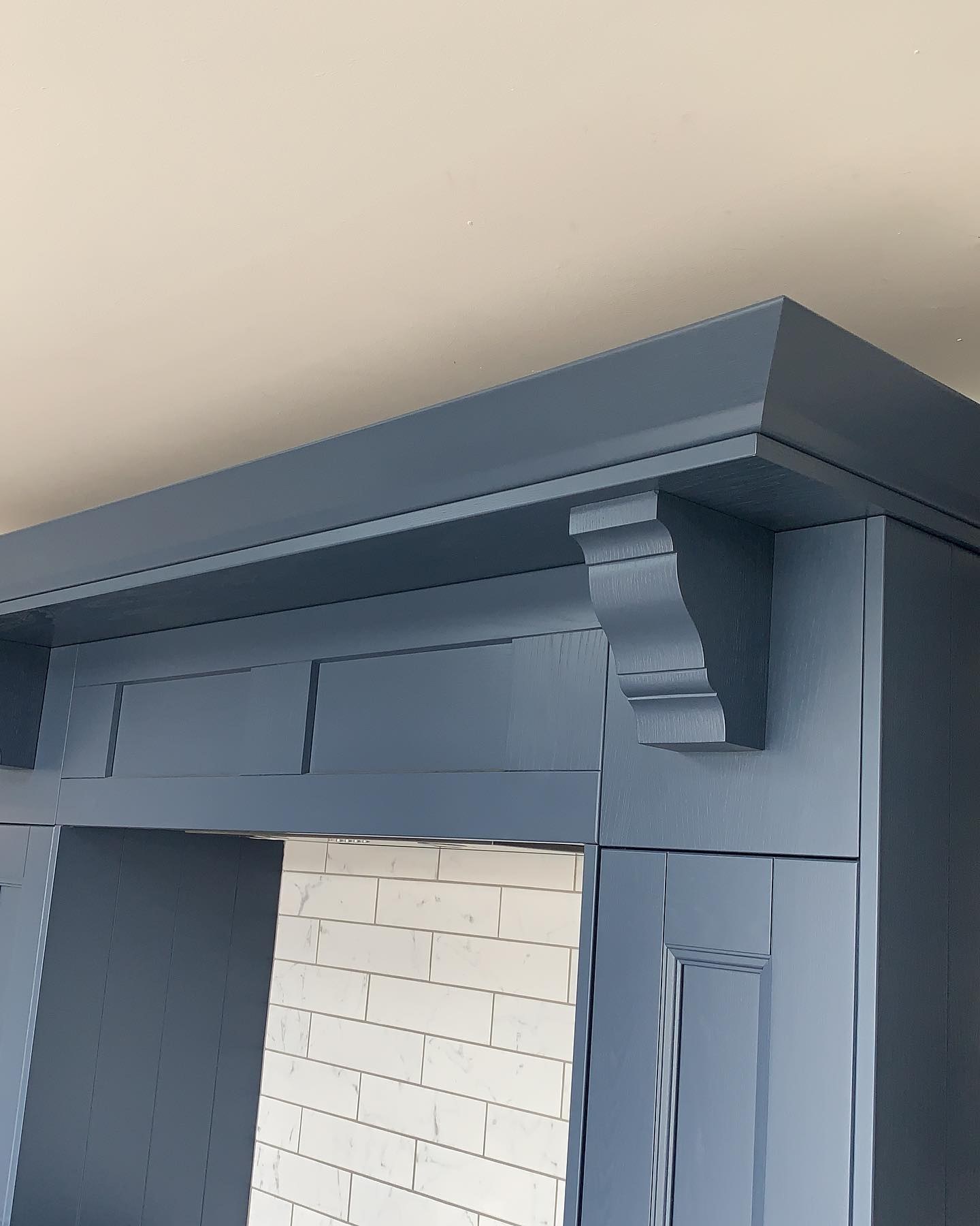 Blue painted cabinetry with a corbel and cornice over white tiles