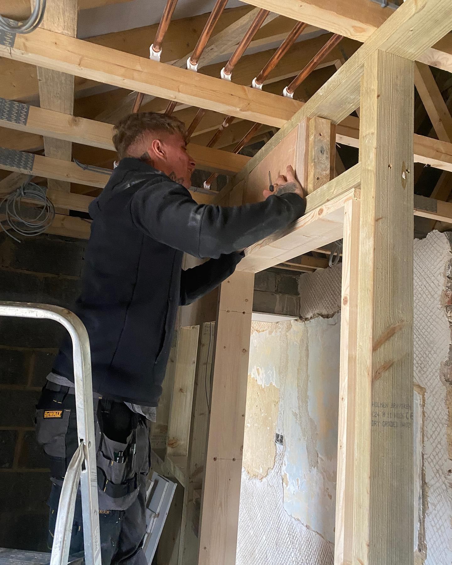 A joiner fixing a timber post in a stripped-out room
